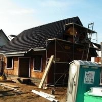 Ein im Bau befindliches Haus mit einem sichtbaren Zaun und einer Toilette im Vordergrund.