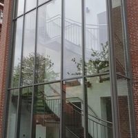 Ein großes Glasgebäude mit Treppen, das modern und einladend wirkt, umgeben von einer urbanen Umgebung.