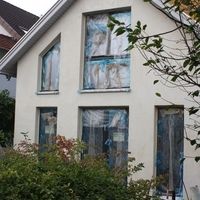 Ein Haus mit zahlreichen Fenstern, umgeben von vielen Bäumen, die eine grüne und einladende Atmosphäre schaffen.