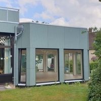 Ein Haus mit einer großen Glastür und einem grünen Dach, das modern und einladend wirkt.
