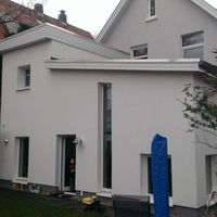 Ein Haus mit einem blauen Sonnenschirm im Garten, umgeben von grüner Rasenfläche und blühenden Pflanzen.