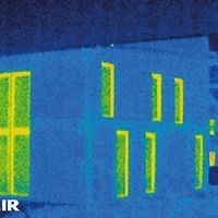Thermografisches Bild eines Hauses mit einem Thermometer, das die Temperaturverteilung anzeigt.
